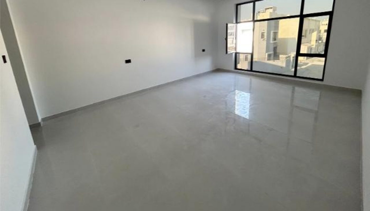 Empty room with white walls, large window, and glossy gray floor; ceiling light fixtures are unfinished.