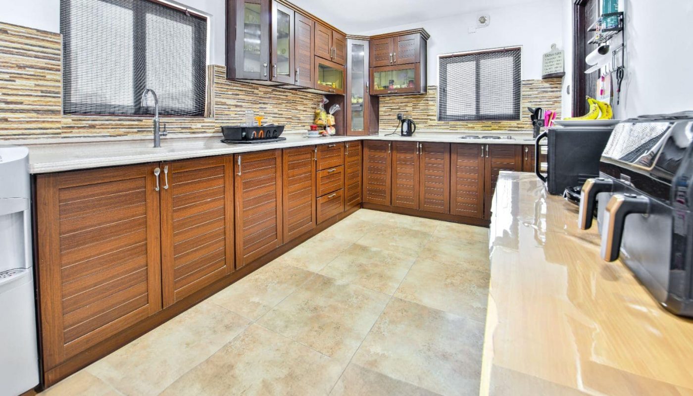 A modern kitchen with wooden cabinets, a refrigerator, countertops with small appliances, and a tiled floor.