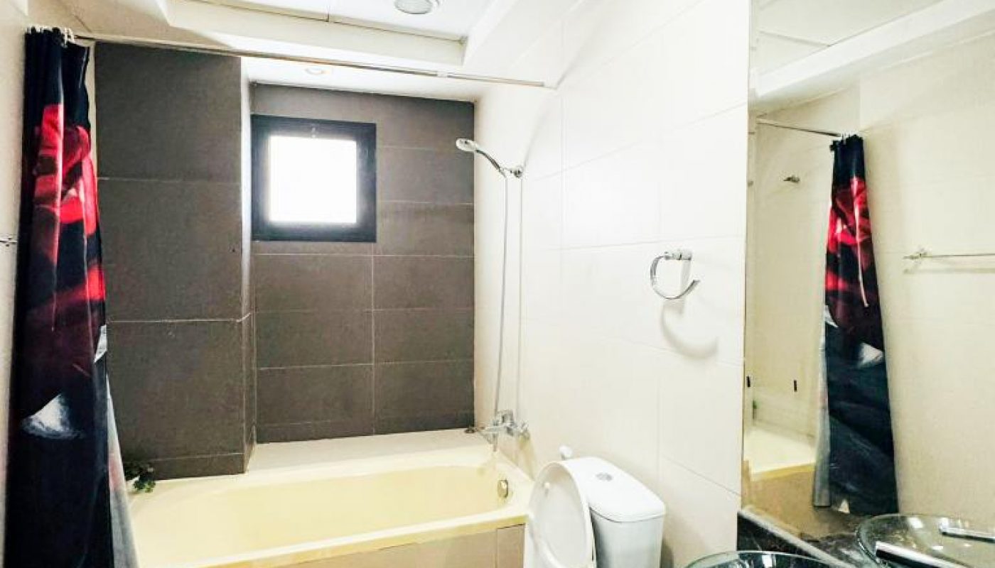 Modern bathroom with a bathtub, toilet, glass vessel sink on a dark countertop, wall mirror, and rose-patterned shower curtain and floor mats. A small window lets in natural light.