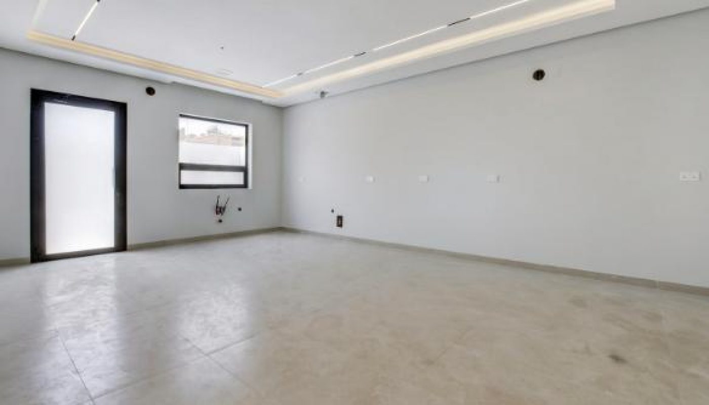 Empty room with light-colored tiled floor, white walls, and a multi-level ceiling with recessed and linear lighting. A door and a window are visible.