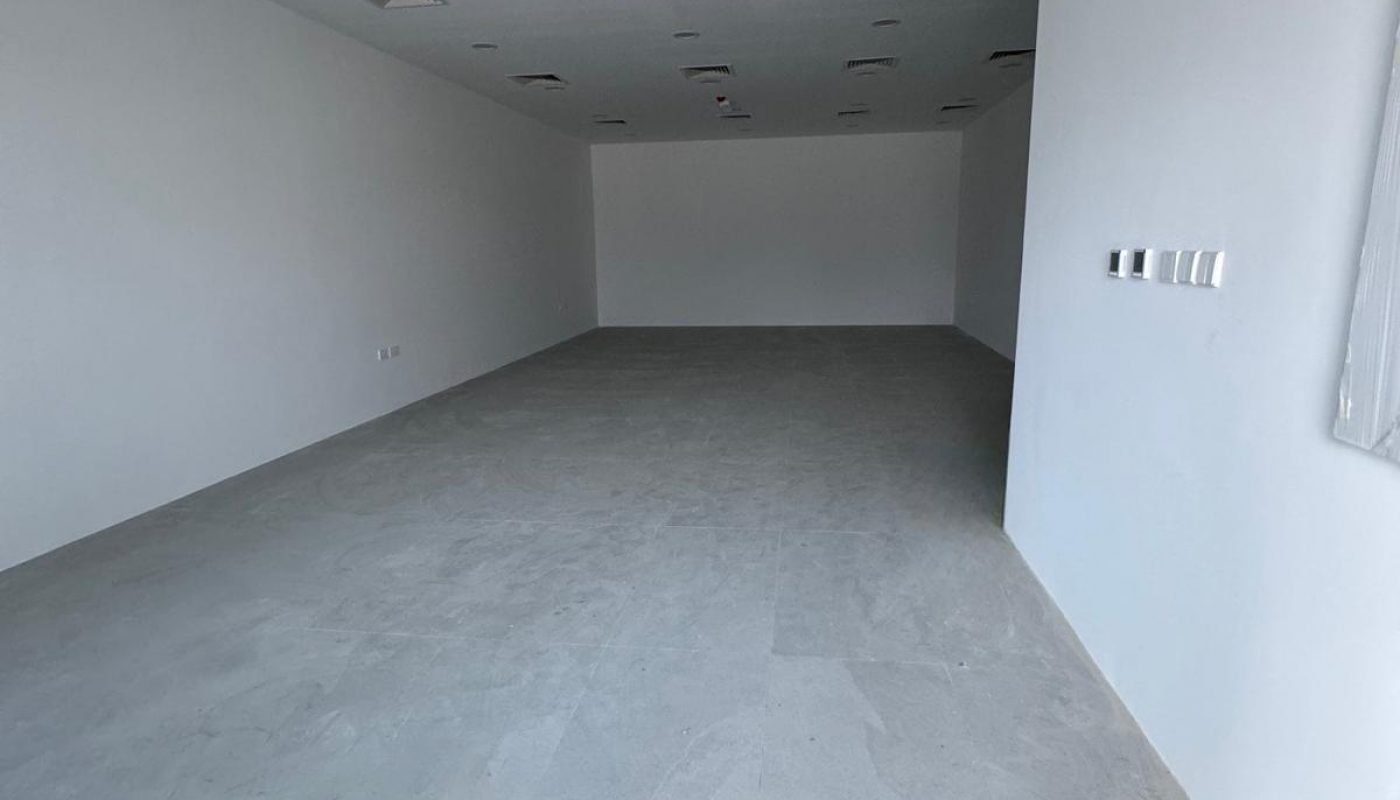 Empty, unfurnished white room with grey tiled floor, white walls, multiple ceiling lights, air vents, and wall switches visible on the right.