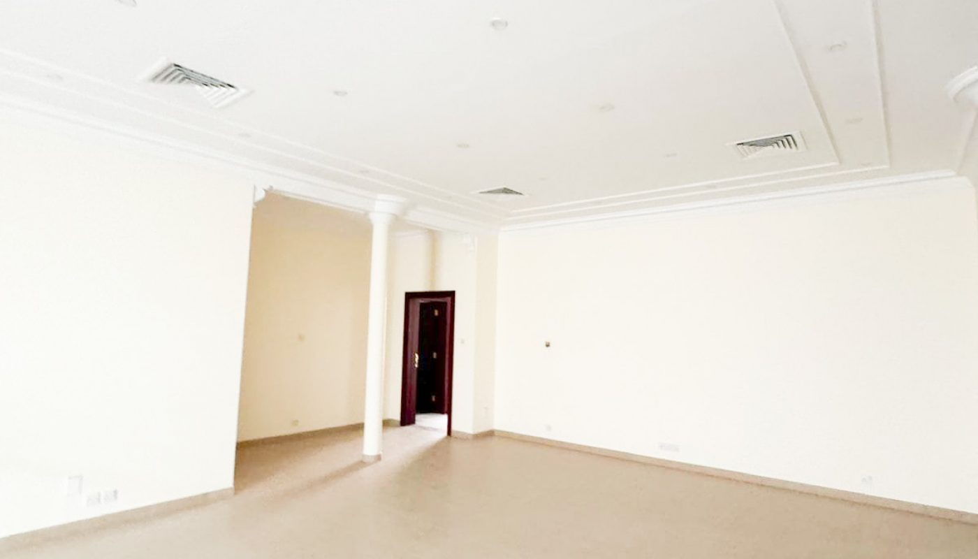 Spacious, empty room with cream-colored walls, tiled floor, white ceiling with vents, two white columns, and a dark doorway in the back.