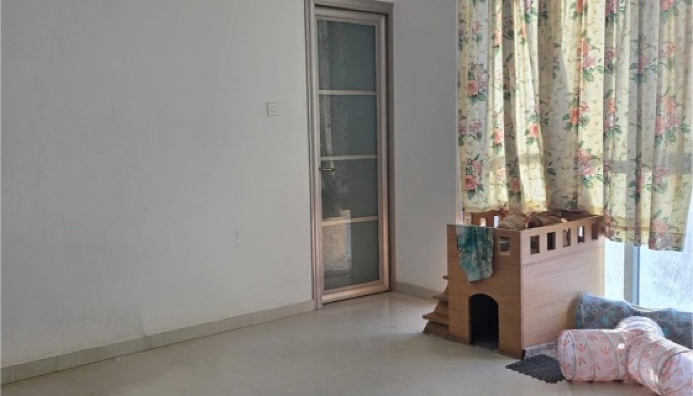 A mostly empty room with tiled floor, a glass door, floral curtains, a wooden pet house, and some cushions by the window.