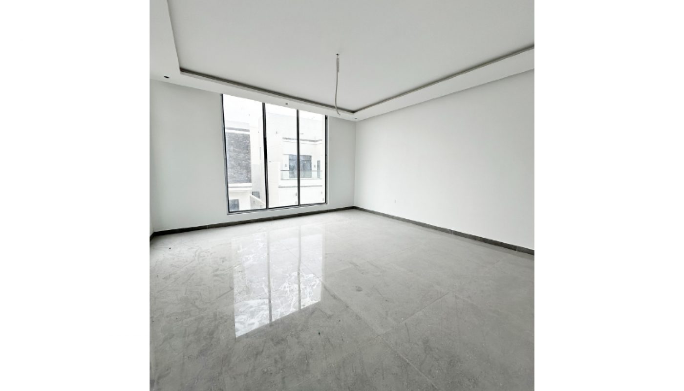 Empty white room with large floor-to-ceiling windows, gray tiled floor, recessed ceiling, and minimal natural light.