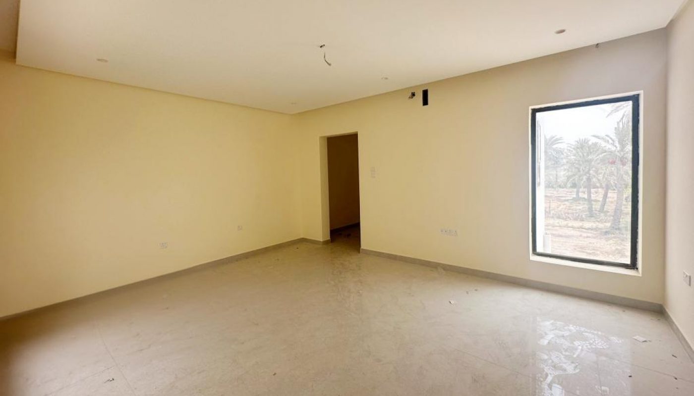 Empty, unfurnished room with cream walls, beige tiled floor, recessed ceiling lights, one large window, and an open doorway; daylight enters through the window.
