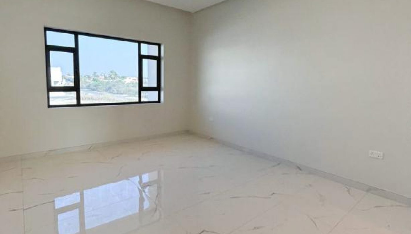 Empty room with large, glossy white marble tile floor, light gray walls, ceiling lights, and a window with an outdoor view.