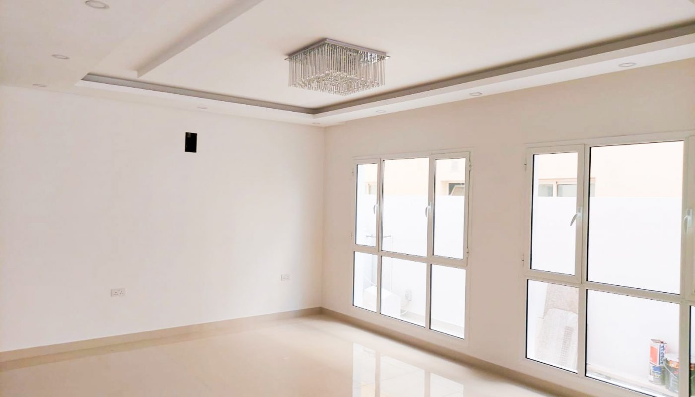 A large empty room with white walls and large windows in a bright 6BR Villa for Sale in Galali with a garden.