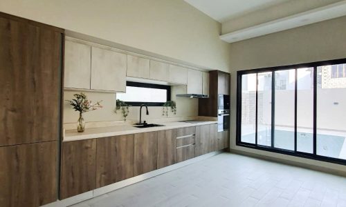 A modern kitchen with wooden and white cabinetry, a black sink, built-in appliances, and large sliding glass doors to the right. The well-lit space benefits from ample natural light and features an auto draft ventilation system for optimal air quality.