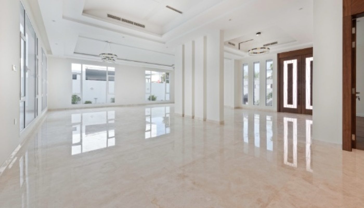 Spacious, empty room with glossy marble floors, white walls, large windows, and double front doors under modern ceiling lights.