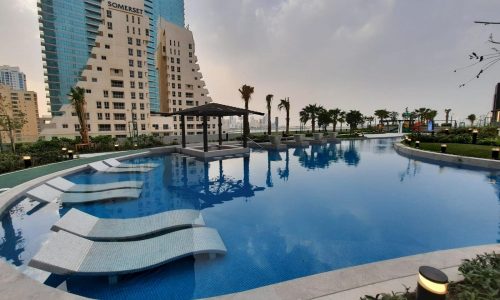 A swimming pool with lounge chairs in front of tall buildings is an Amazing recreational feature offered for Sale in Juffair.