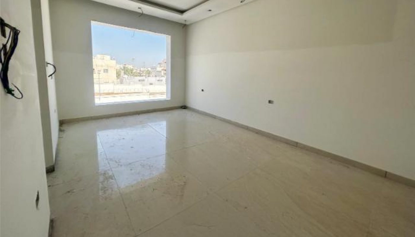 Empty, unfurnished room with tiled floor, large window letting in daylight, and unfinished ceiling with exposed wiring.