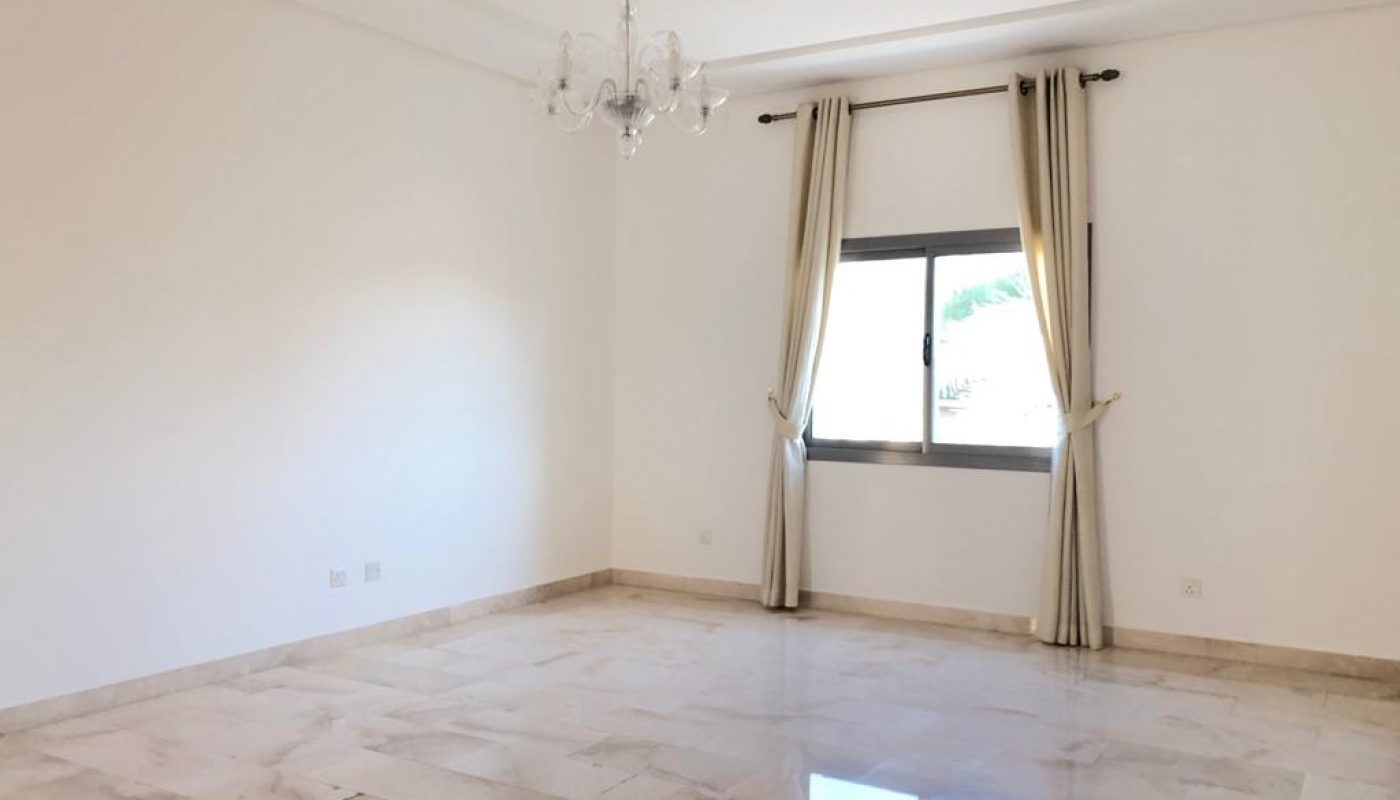 Empty living room with shiny tiled floor, white walls, and a window dressed with beige curtains under a chandelier.