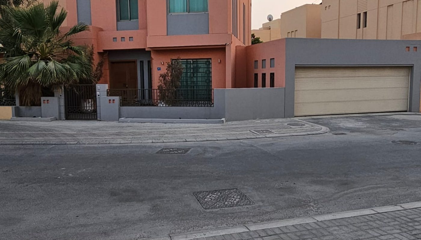 A modern two-story house with peach and gray exterior walls, large windows, a gated entrance, and an attached two-car garage, situated on a quiet, paved street.