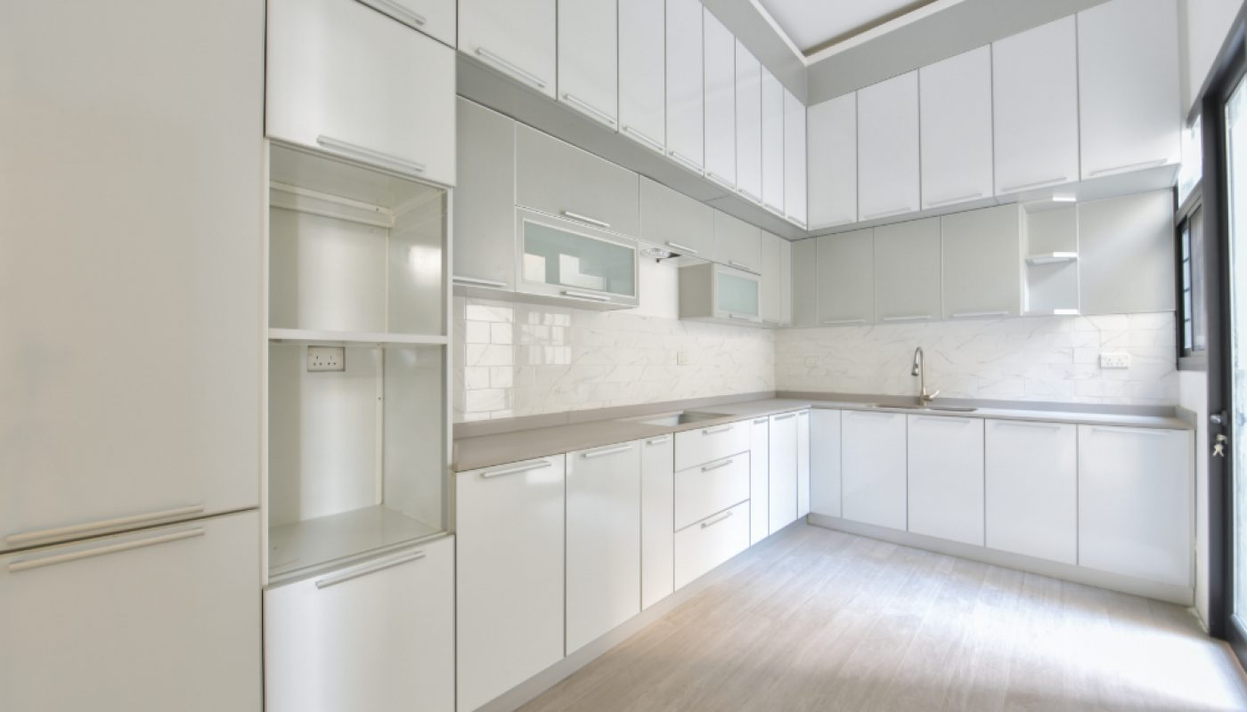 Modern kitchen with white cabinets, light wood flooring, tiled backsplash, and under-cabinet lighting. The space appears clean and empty with natural light coming from a window.