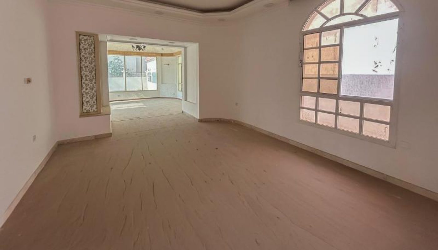 Unfurnished, empty room with a large arched window, recessed ceiling, and an open doorway leading to a sunlit adjoining space.