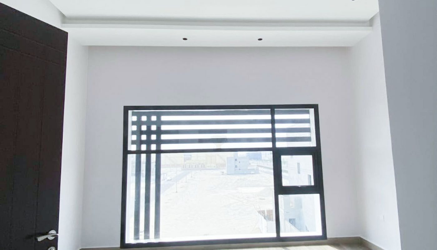 Empty room with light-colored walls, wood flooring, a dark door on the left, and a large window letting in natural light with a view outside.