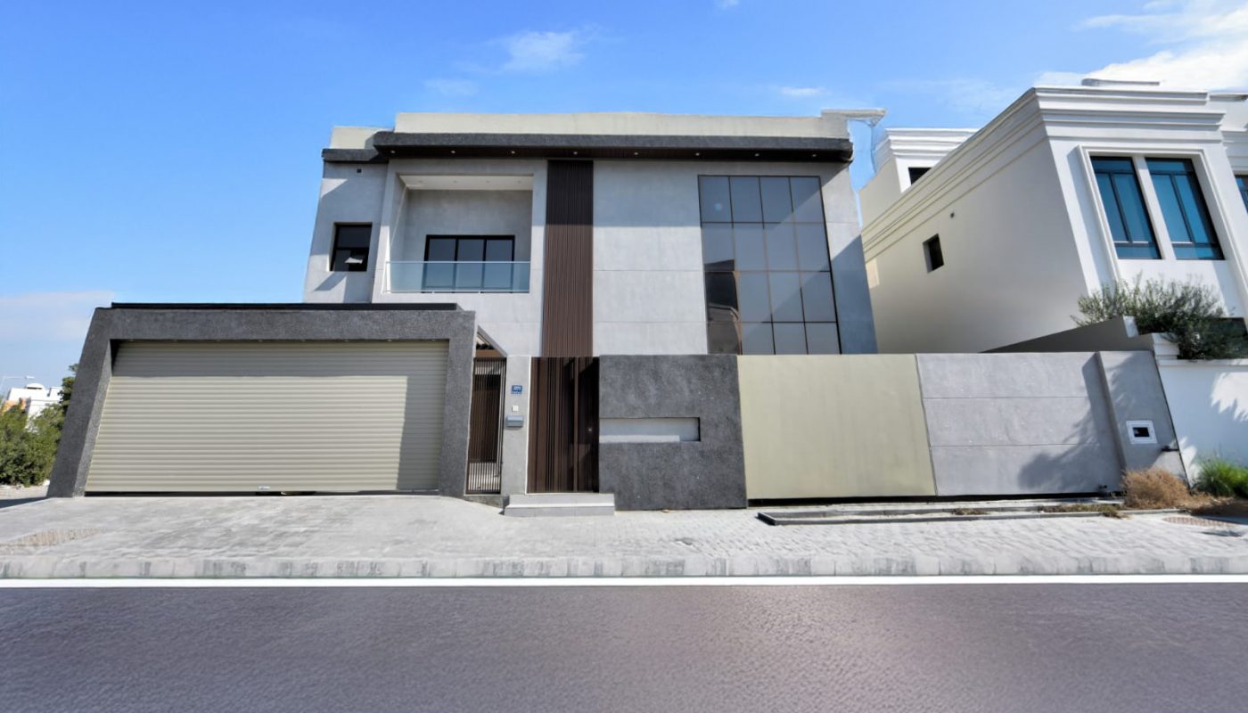 Modern two-story house with a flat roof, large glass windows, gray exterior walls, and an attached garage, situated on a paved street under a clear blue sky.