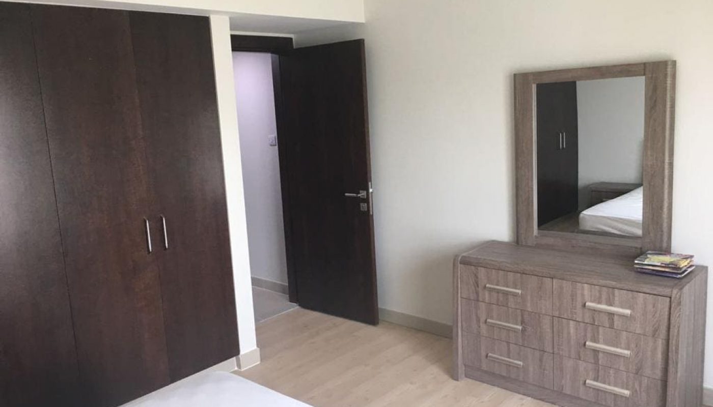 A fully furnished bedroom in an apartment, complete with a dresser and mirror available for rent.