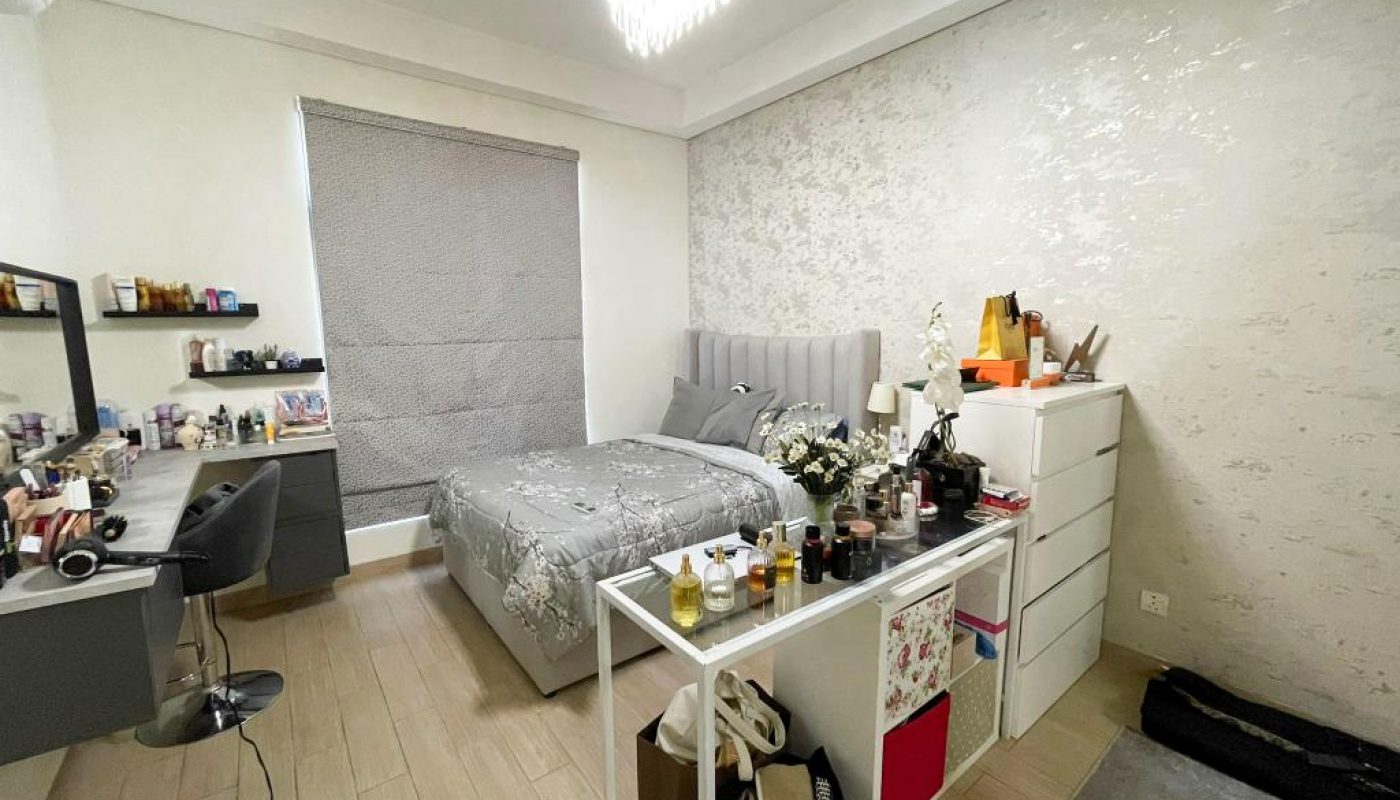 A neatly arranged bedroom with a bed, dresser, vanity table with a chair, and a glass-top table displaying various cosmetics and accessories.