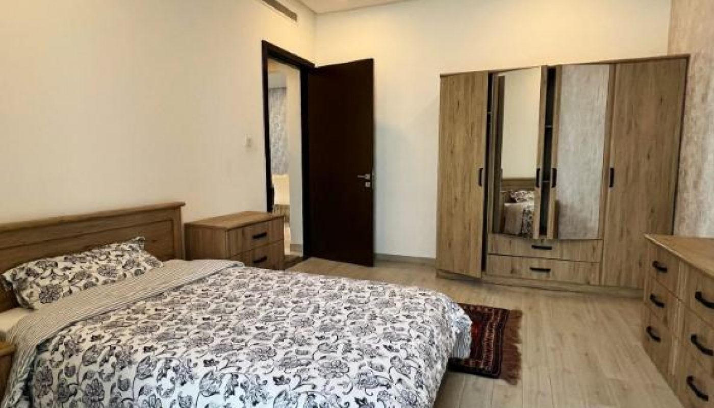 A neatly made bed with floral bedding in a modern bedroom featuring light wood furniture, a wardrobe with mirrors, and light-colored flooring.