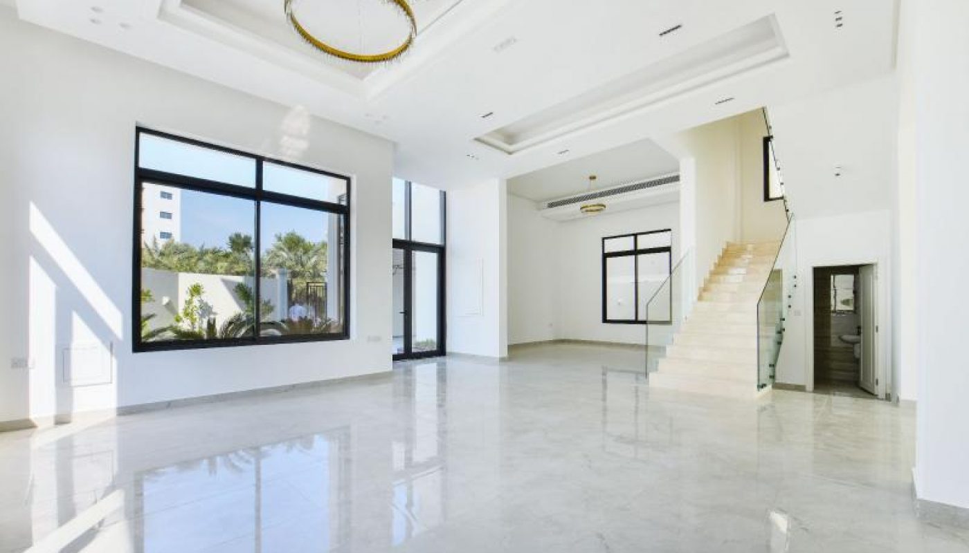 Spacious, modern living room with large windows, marble floors, white walls, high ceilings, gold chandeliers, and a staircase leading to an upper level.