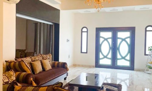 A wonderful living room with couches and a chandelier in a 5BR Villa for Sale in Muharraq with a garden.