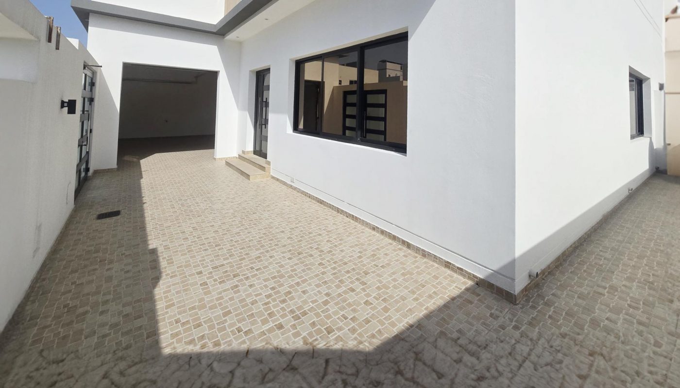 A modern white house with large windows and a paved driveway wraps around the side of the building under a clear sky.