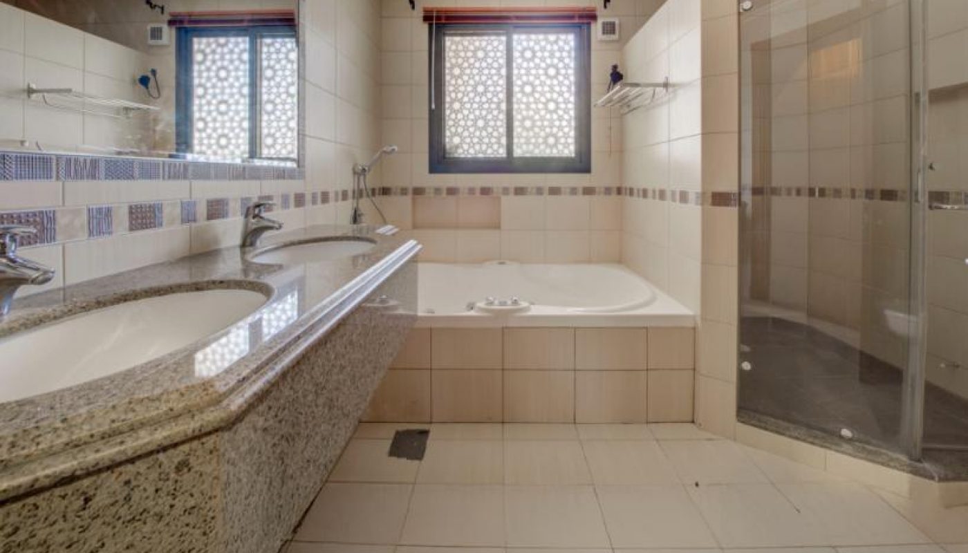 Modern bathroom with double sinks, a large mirror, a built-in bathtub, a glass-enclosed shower, and a window with decorative grilles.