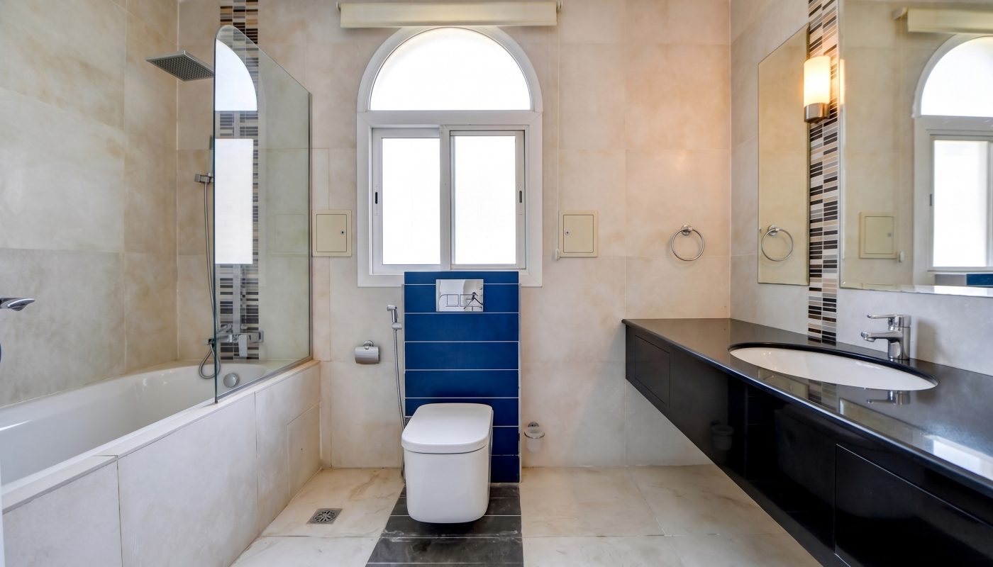 Modern bathroom with a bathtub, square toilet, blue accent tiles, large mirror, black vanity, and a window with an arched top.