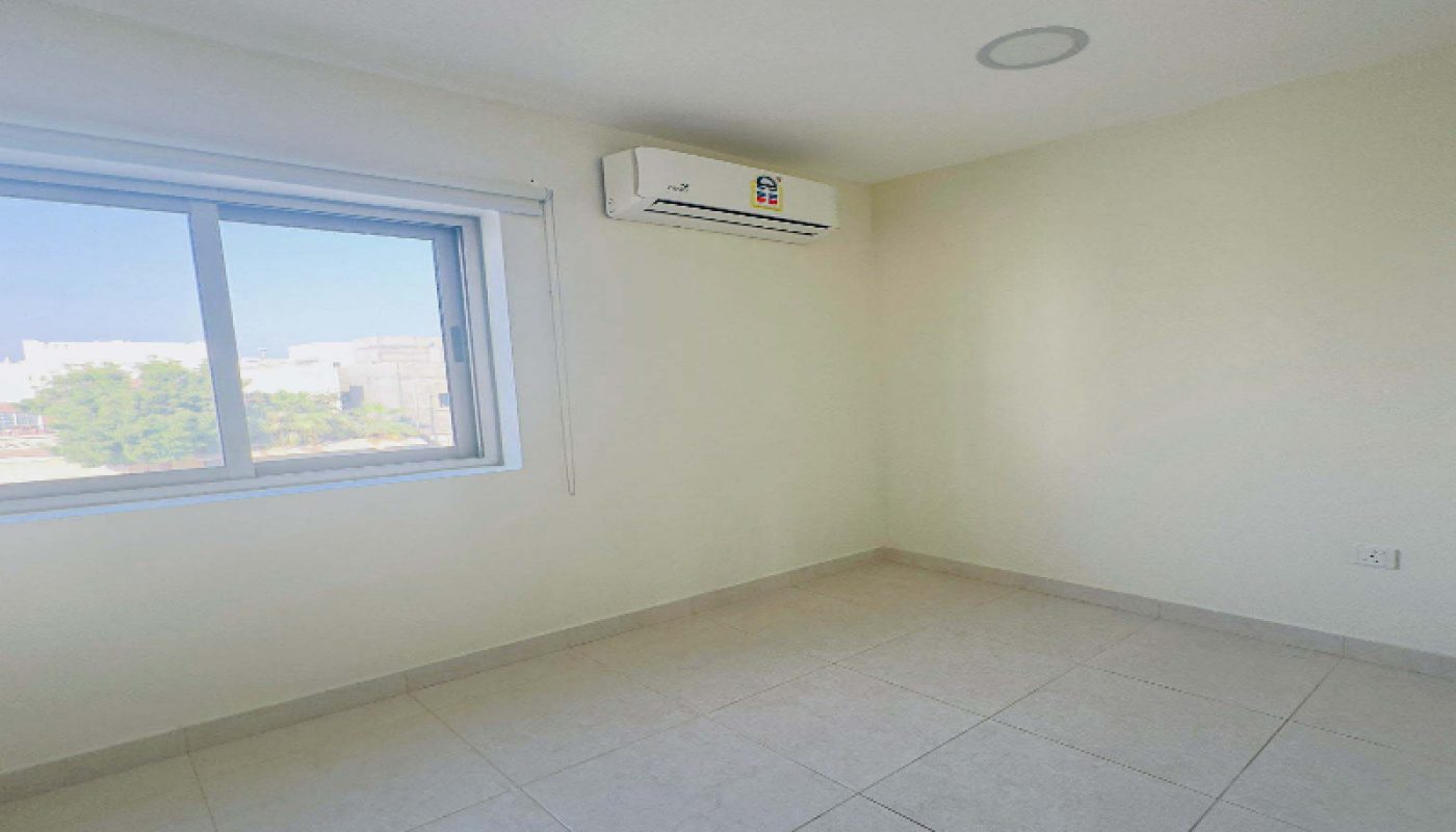 Empty room with tiled floor, cream-colored walls, a window with a city view, and a wall-mounted air conditioning unit.