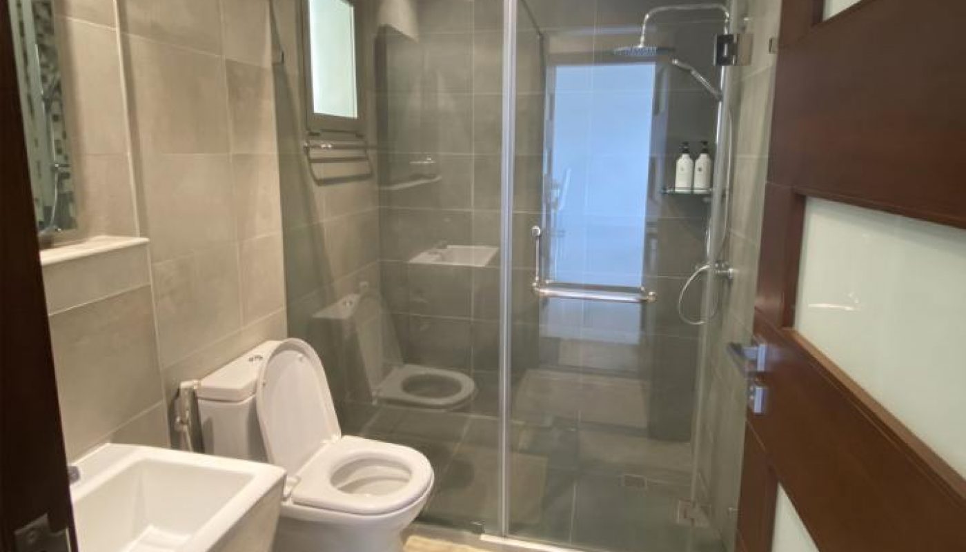 Modern bathroom with a glass-enclosed shower, toilet, sink, wall mirror, towels, and bath mats on a tiled floor.