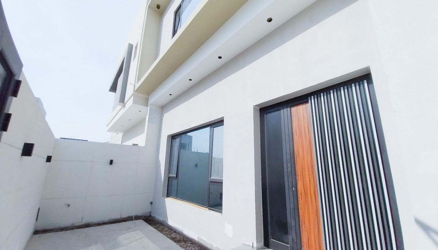 A modern, two-story white house with large windows, a black and wooden front door, and a small concrete front yard.