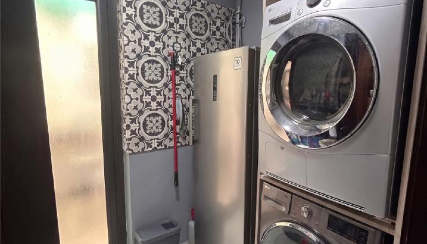 Laundry room with stacked LG washer and dryer, stainless steel refrigerator, trash can, and patterned wallpaper.