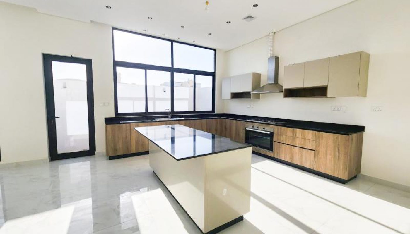 Modern kitchen with wood and beige cabinets, black countertops, a large island, built-in oven, and large windows letting in natural light.