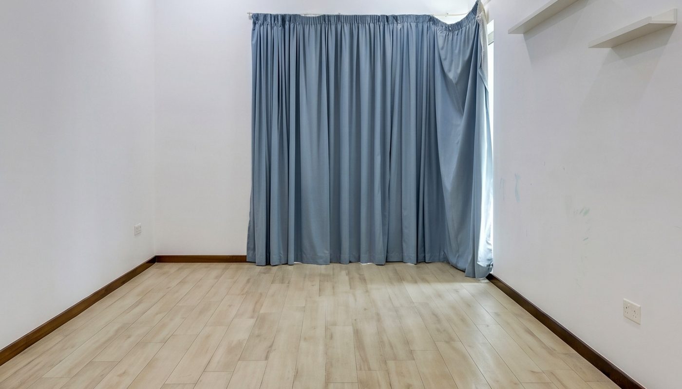 Empty room with light wood flooring, white walls, blue curtains covering a window or door, and two small white shelves on the right wall. Ceiling lights are on.