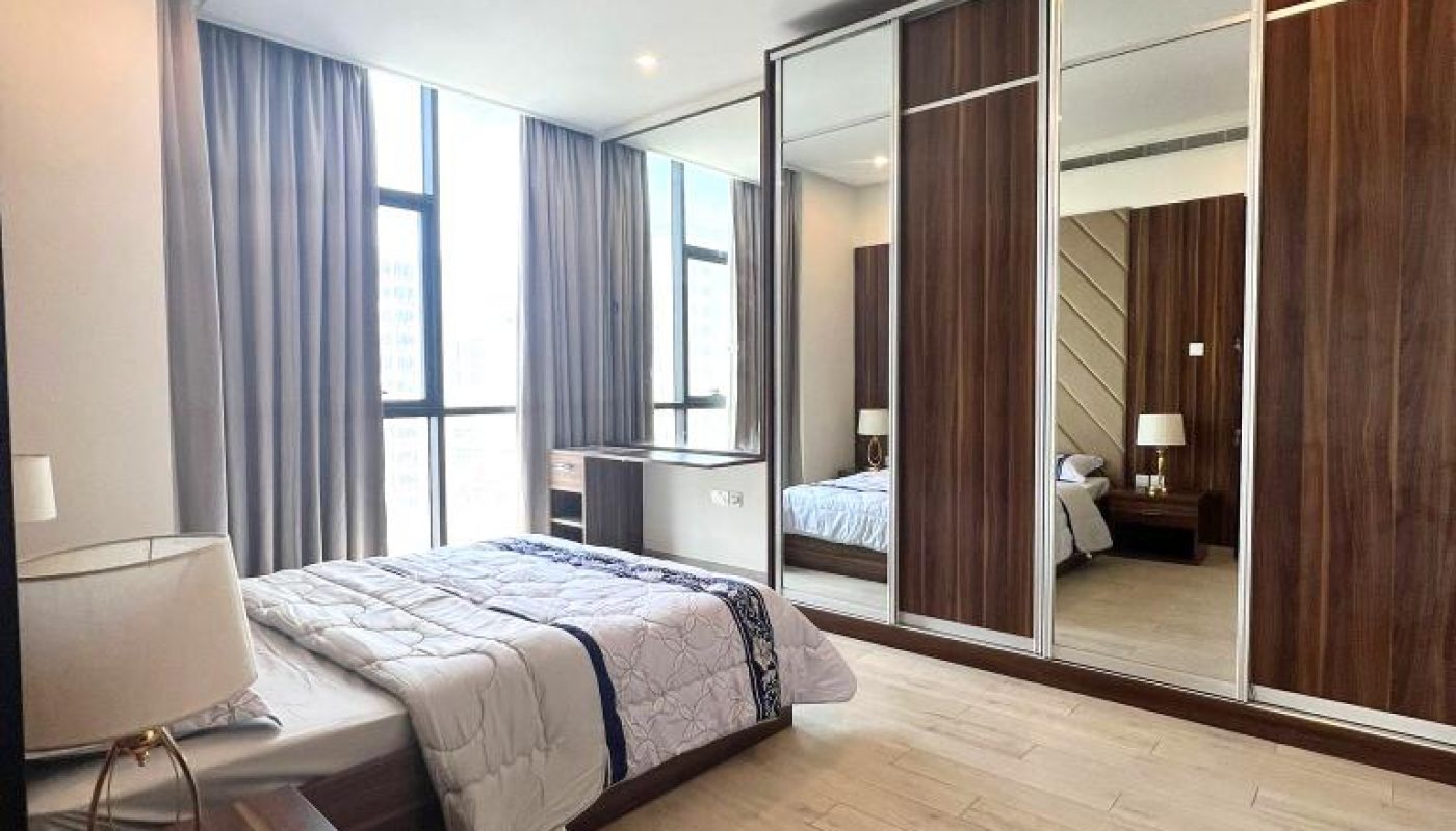 Modern bedroom with a single bed, bedside table, lamp, large mirrored wardrobe, wood flooring, and floor-to-ceiling window with curtains.