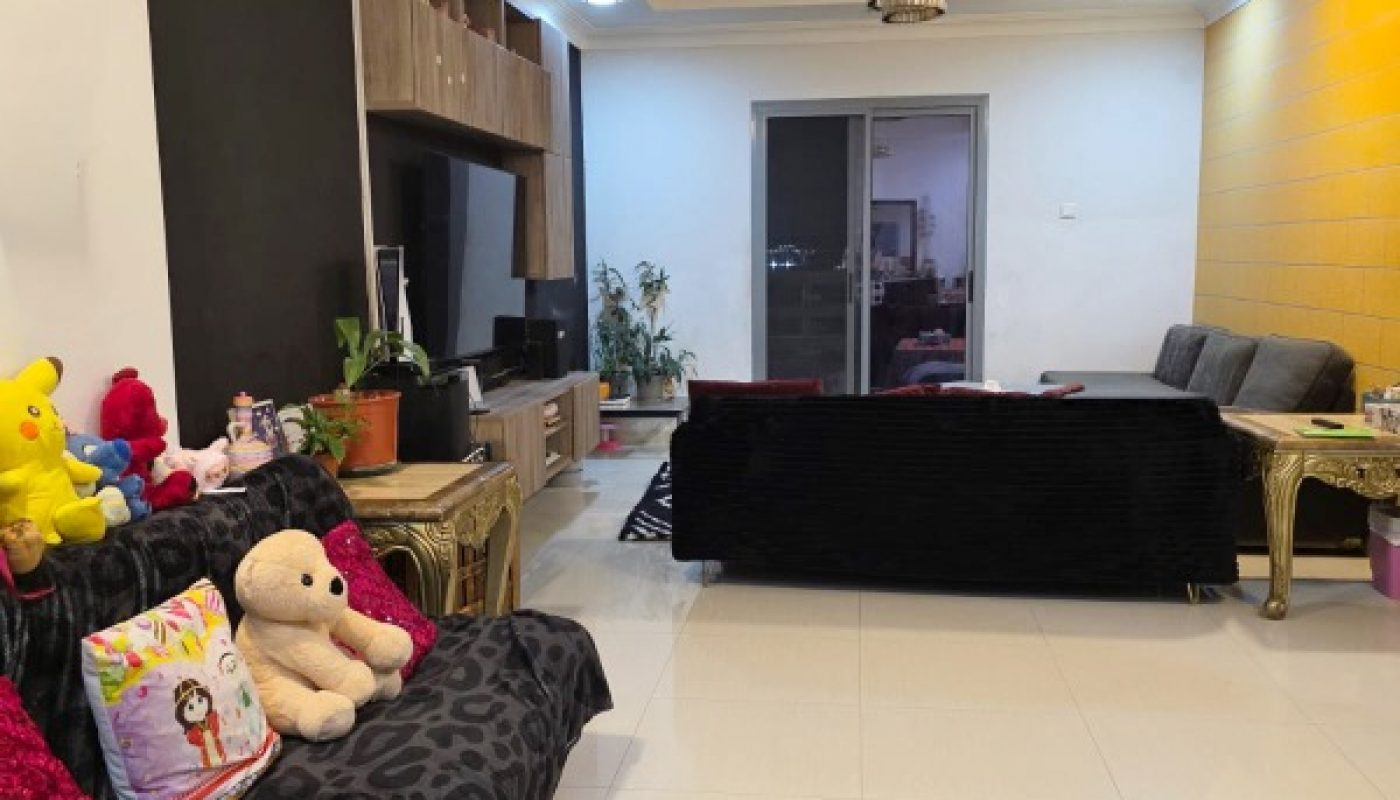 A modern living room with two black sofas, colorful cushions and plush toys, a TV unit, indoor plants, and a sliding glass door leading to another room.