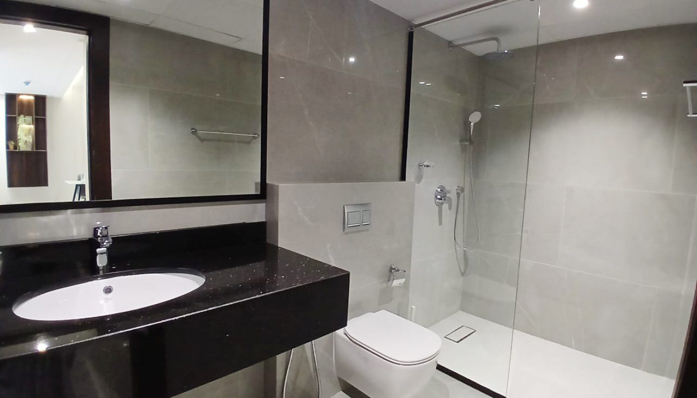 Modern bathroom in Amwaj Islands with a large mirror, black countertop sink, wall-mounted toilet, and a walk-in glass shower enclosure with rainfall showerhead—perfect for stylish living in Freehold apartments.