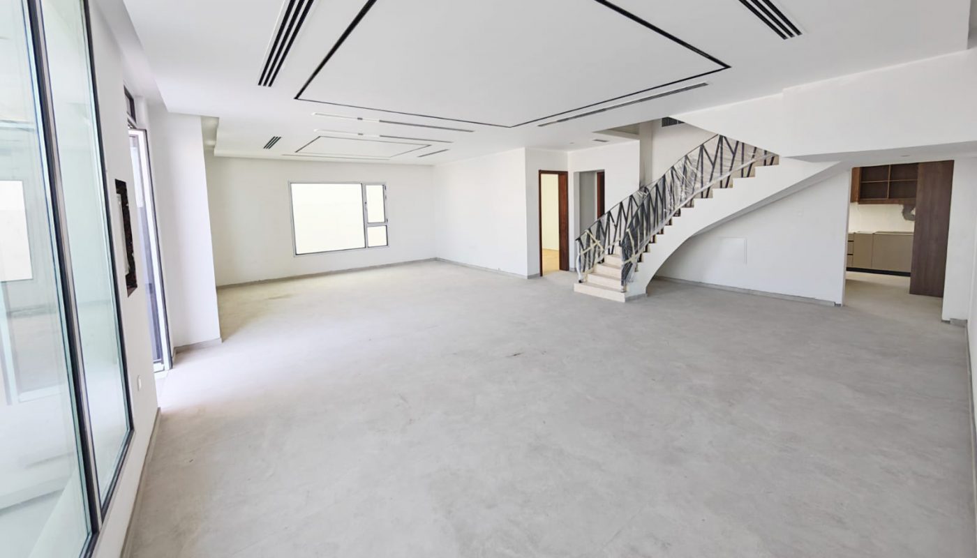 Spacious, empty modern room with large windows, a white staircase with metal railing, and an open entry to an adjacent kitchen area.
