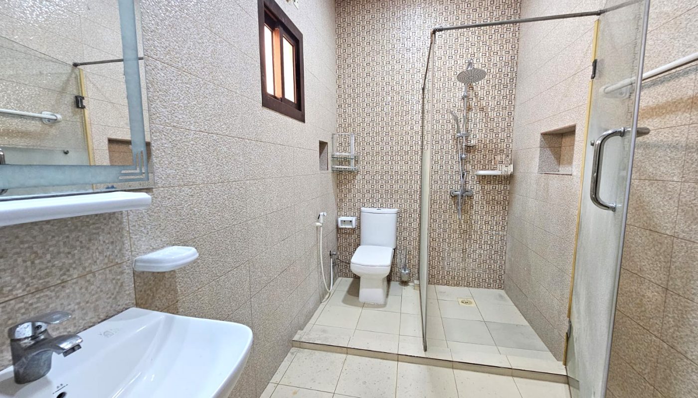 A modern bathroom with a wall-mounted sink, toilet, glass-enclosed shower, beige tiles, a small window, and a mirror above the sink.