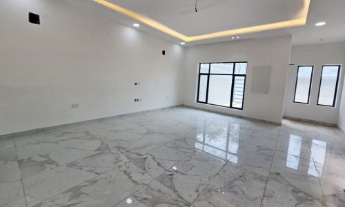 A spacious room in a luxurious villa with a white ceiling featuring recessed lighting, marble flooring, and large windows letting in natural light.