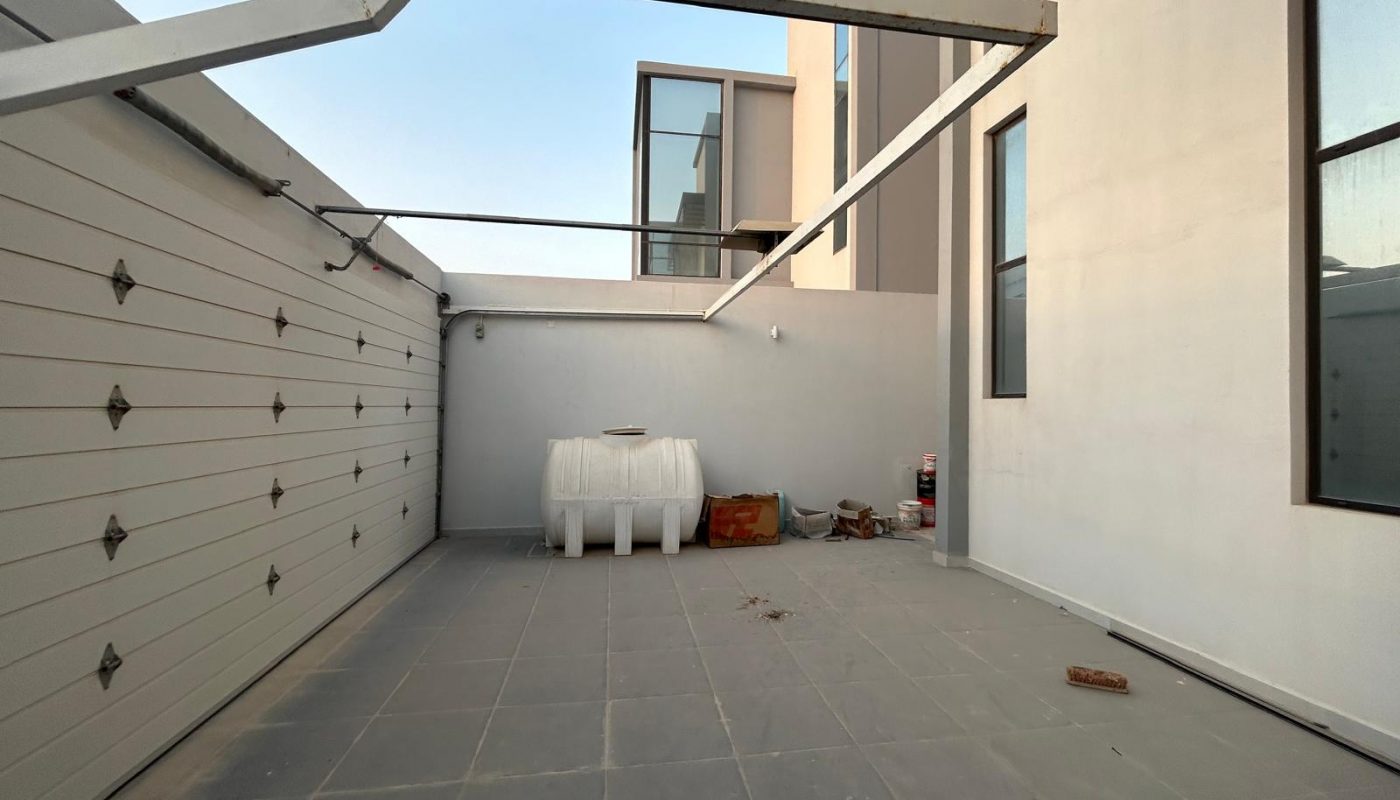 Gated outdoor area with tiled floor, a large white tank, some scattered items, and light-colored modern building walls.