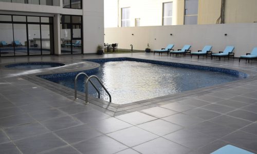 For sale, a fully furnished 1BR unit in a building with a swimming pool and lounge chairs.