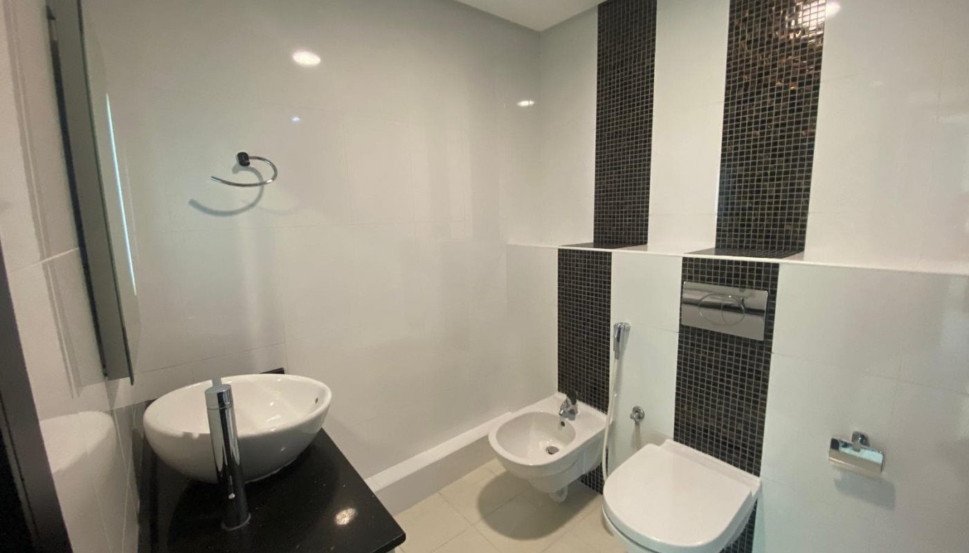 Modern bathroom with a wall-mounted toilet, bidet, white vessel sink on a black counter, and vertical black tile accents on the wall.