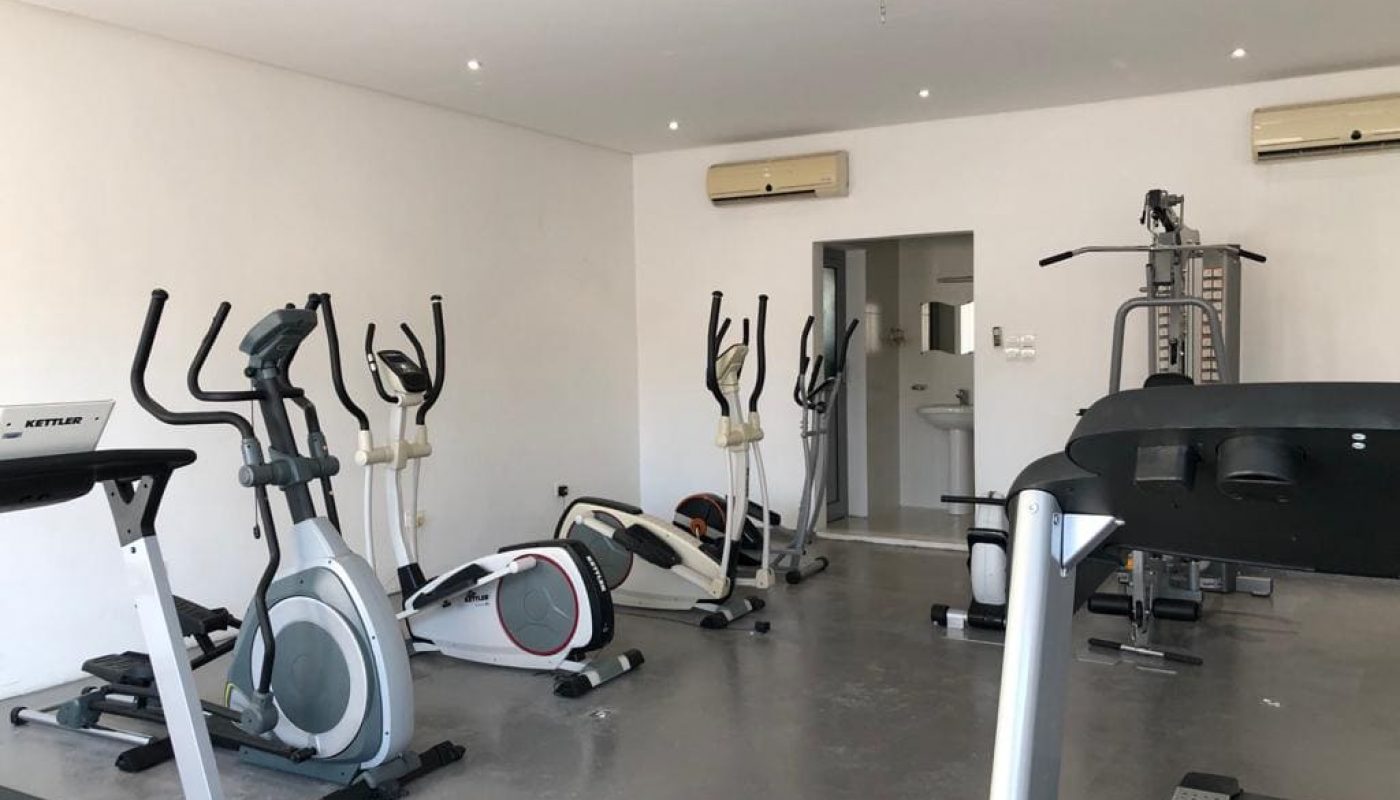 A small, modern home gym equipped with treadmills, elliptical machines, and a weight training station, featuring a minimalist white decor.