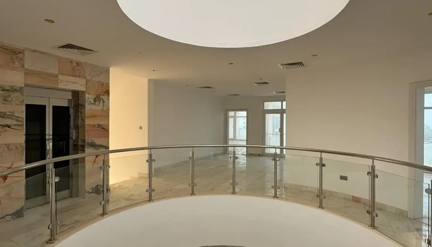 A modern, spacious interior with a circular skylight, glass railing, marble floors, and large windows letting in natural light.