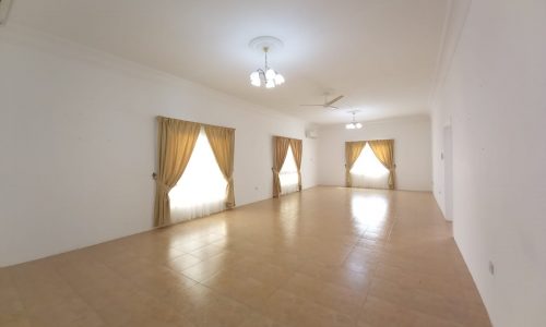 Empty, brightly lit room with white walls, tiled floor, three windows with gold curtains, and two ceiling fans.