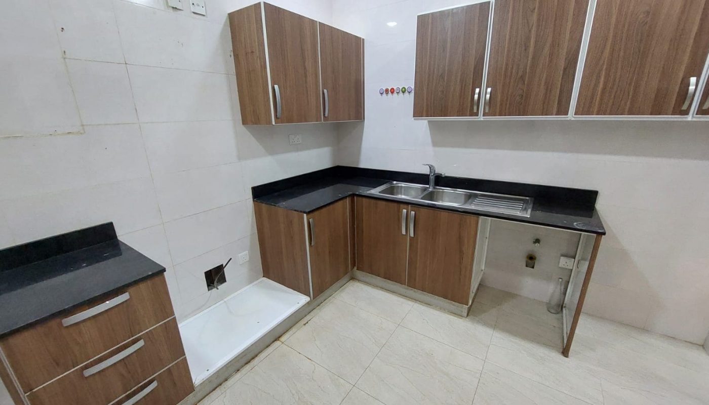 Kitchen with wooden cabinets, dark countertops, stainless steel sink, and white tiled walls and floor.