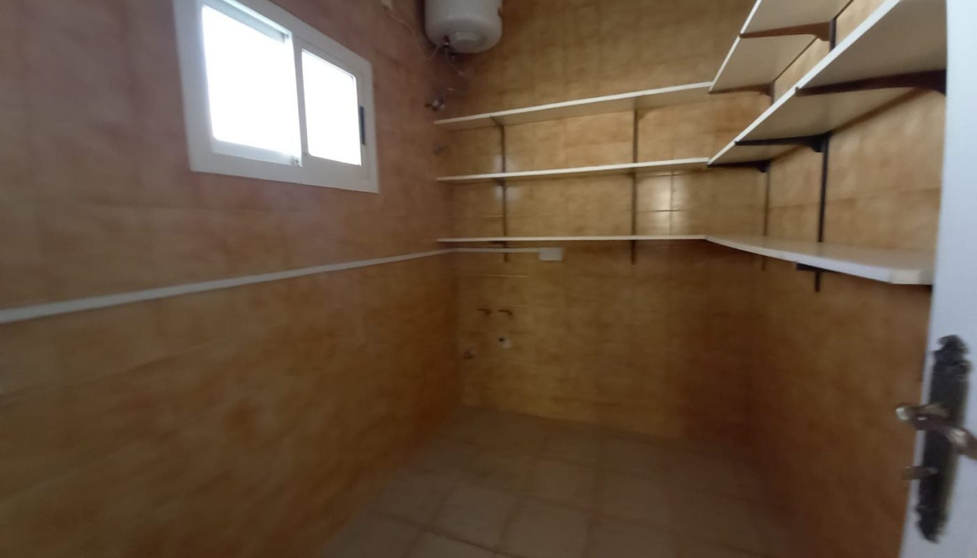 Interior of an empty storage room with beige tiled walls, multiple white shelves, and a small window.