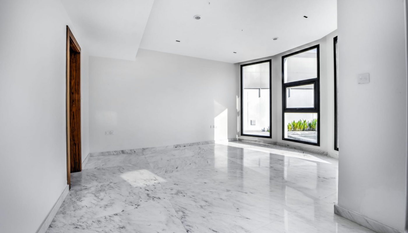 Empty room with white marble flooring, white walls, large black-framed windows, and a wooden door on the left.